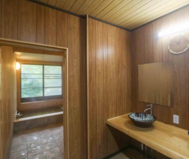 Wood-paneled washroom with ceramic basin and wooden countertop, doorway to tiled bathing area with window at Senzairou Gifu