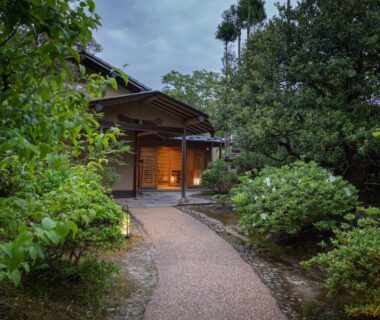 Gravel garden path leading to softly lit wooden ryokan entrance framed by lush greenery in Niigata