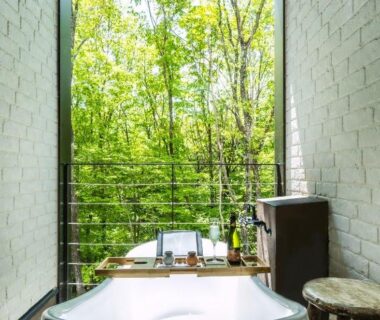 Freestanding bathtub facing green forest through floor-to-ceiling window, Shelter Garden Nikko, Tochigi