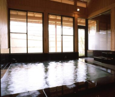 Large indoor onsen bath with wooden interior and shoji-style windows at Shibu Hotel Nagano