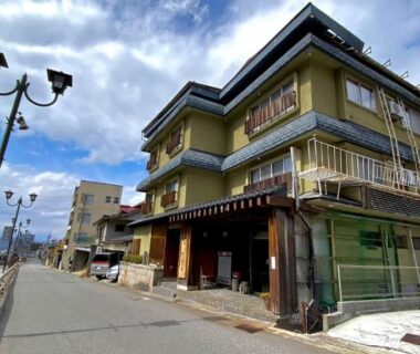 Three-story ryokan by the river with balconies, street lamps and a riverfront walkway in Shibu Onsen, Nagano