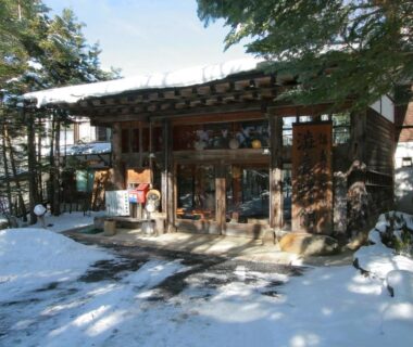 Snow covered entrance of Shibu Tatunokan in Nagano with surrounding trees