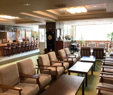 Bright lounge with wooden chairs, low tables and counter by large windows at Shiga Ichii Hotel Nagano