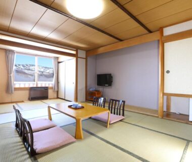 Traditional tatami room with low table, floor cushions, sliding doors and window overlooking nearby rooftops at Shiga Ichii Hotel, Nagano.