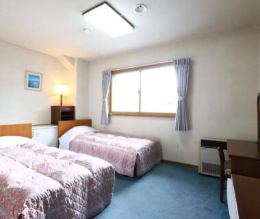 Two single beds with desk, window and curtains in Shiga Ichii Hotel room Nagano