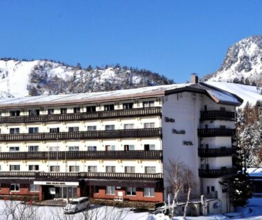Snow-covered exterior of Shiga Palace Hotel with balconies and mountain backdrop in Nagano