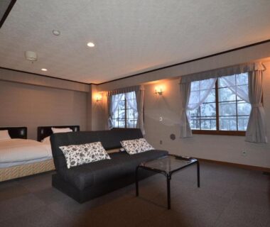 Twin beds and sofa seating with windows and low table at Shiga Palace Hotel in Nagano