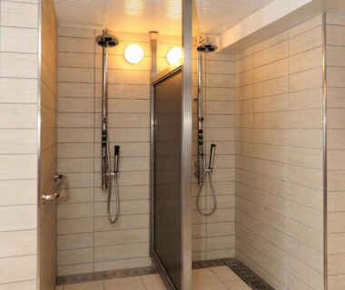 Tiled communal shower stalls with handheld showerheads and partitions at Shiga Park Hotel in Nagano