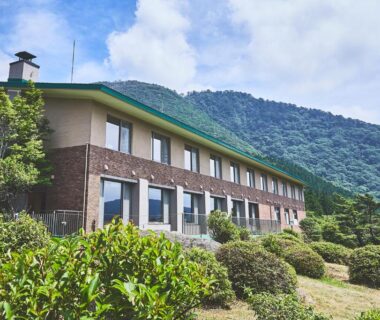 Two-story ryokan building with manicured shrubs and mountain backdrop at Shiki Resort Hakone Style, Kanagawa