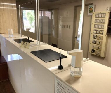 Reception counter with acrylic partitions, bell, sanitizer and key boxes at Shiki-no-Yado Fujisan, Yamanashi