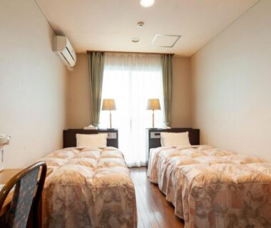 Compact twin room with twin beds, bedside lamps, air conditioner and wooden floor at Shikino Mori, Kumamoto, Kyushu