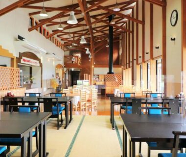 Spacious communal dining room with wooden beam ceiling, tables on tatami and large windows at Shikino Mori, Kumamoto
