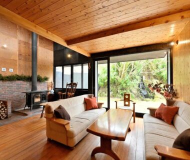 Wood-paneled lounge with sofas, fireplace and large window overlooking garden at Shikinosato Hanamura Kumamoto