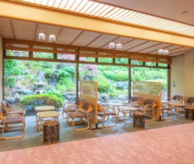 Seating area with rattan chairs and low tables facing a manicured garden at Shikitei Morioka TsunagiOnsen, Iwate