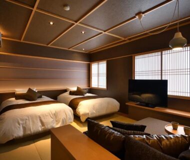 Spacious tatami room with twin beds, low wooden table, shoji screens and lounge seating at Shima Onsen Yoshimoto Gunma
