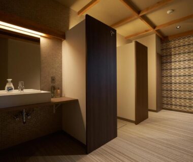 Warmly lit communal wash area with sinks, wooden partitions and patterned wall at Shima Onsen Yuzuriha, Gunma
