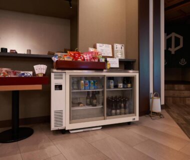 Small refreshment area with refrigerated drinks, packaged snacks, electric kettle, and noren entrance at Shima Onsen Yuzuriha in Gunma