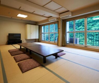 Spacious tatami room with low table, floor cushions and large windows overlooking forest at Shima Onsen Yuzuriha, Gunma