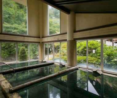 Glass-walled indoor onsen pools with stone surrounds and garden views at Shima Tamura in Gunma, Japan