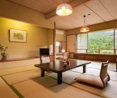 Traditional tatami room with low table, seating and large window overlooking green hills at Shima Tamura, Gunma