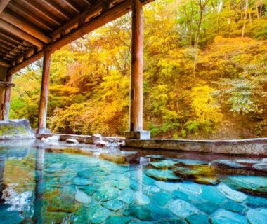 Roofed outdoor onsen with stone floor and vivid autumn foliage at Shima Yamaguchikan, Gunma