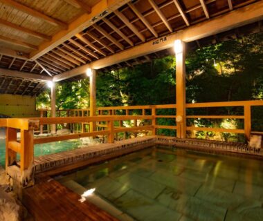 Wooden sheltered onsen bath with stone basin and warm lantern lighting at Shima Yamaguchikan, Gunma