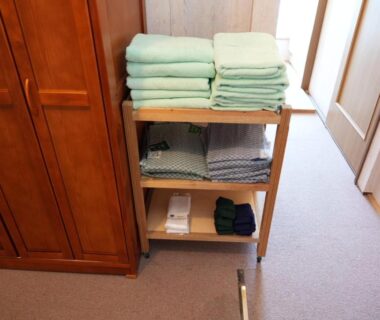 Stacked bath towels and folded yukata on wooden shelf beside wardrobe in a ryokan room