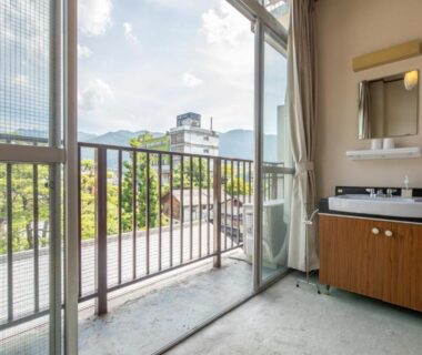 Open sliding glass door to balcony with railing, room washbasin cabinet and distant mountain view in Nagano