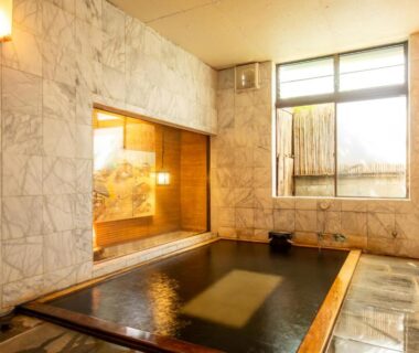 Marble-tiled indoor onsen bath with wooden edging and window at Shimaya in Nagano