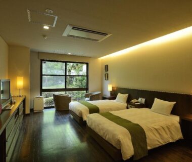 Bright room with twin beds, wooden floor, lounge chairs by large window overlooking green trees at Shimoda Central Hotel Shizuoka