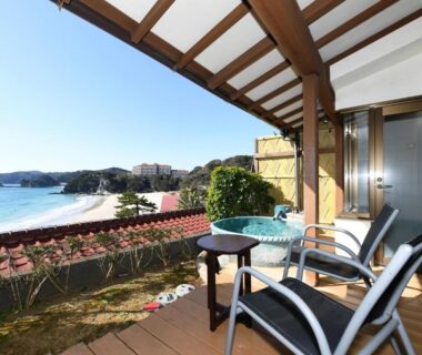 Wooden deck balcony with chairs, outdoor soaking tub and sandy bay view at Shimoda Yamatokan, Shizuoka