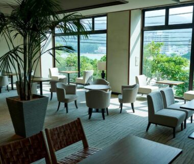 Bright lounge with armchairs and tables, large windows overlooking greenery at Shin Kaikatei Izumi in Shizuoka