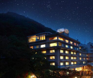 Night view of illuminated Shinki ryokan building against mountain and starry sky in Gunma, Kantō, Japan