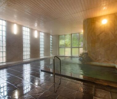 Indoor onsen bath at Shinseikan with stone wall, tiled floor and large windows Iwate Tohoku