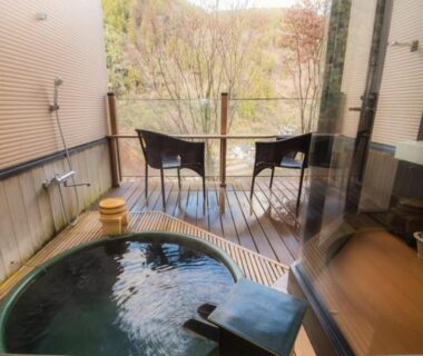 Circular wooden balcony onsen with two chairs overlooking a wooded hillside at Shinshiyo, Ōita, Kyūshū