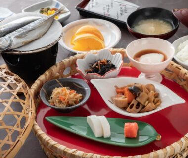 Assorted ryokan breakfast with grilled fish, rice, miso soup, pickles, and small vegetable dishes on a woven tray