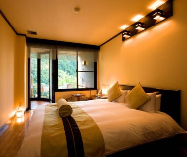 Western-style bed with rolled towel, soft lighting, seating area and garden view through sliding glass doors