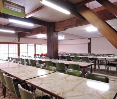 Large communal dining room with long tables, green chairs and exposed timber beams at Shintaku Sanso in Nagano