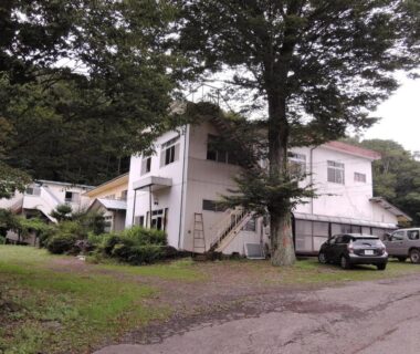 White two-story ryokan exterior with parked cars and trees at Shintaku Sanso, Nagano, Chūbu, Japan