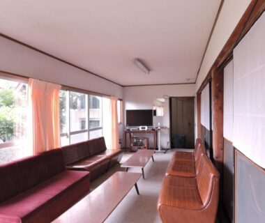 Long sitting area with sofas, low tables, shoji screens and large windows at Shintaku Sanso, Nagano