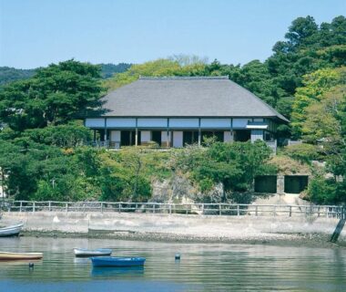 Traditional Japanese ryokan building with broad roof overlooking calm waterfront and moored boats in Miyagi, Tōhoku
