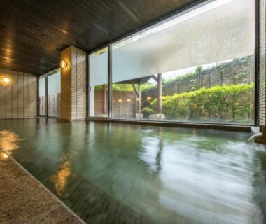 Serene indoor onsen with floor-to-ceiling window and stone rim at Shintomi-tei, Miyagi, Tōhoku