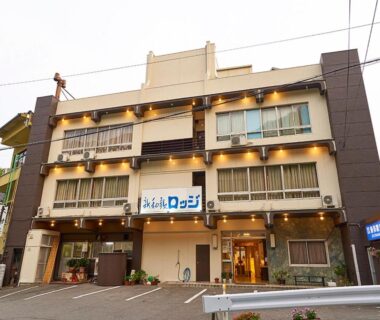 Three-story ryokan facade with lit balconies, entrance and small parking area in Wakayama