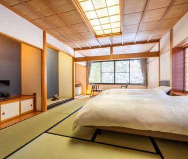 Tatami room with low beds, shoji screens and window overlooking trees at ShirabuOnsen Higashiya, Yamagata
