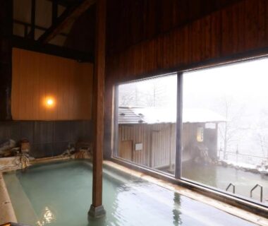 Wooden indoor onsen bath with large window and misty exterior at Shirafune Grand Hotel Nagano