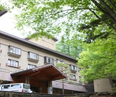 Exterior view with wooden entrance canopy, balconies and surrounding green trees at Shirafune Grand Hotel, Nagano, Chūbu, Japan