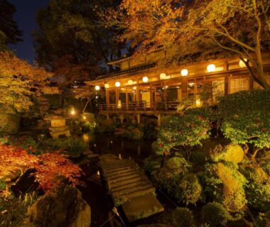 Night view of Shiragiku lit wooden ryokan with maple foliage and stone garden in Ōita