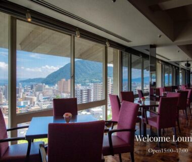 Lounge seating and tables by large windows at Shiragiku overlooking Ōita city skyline and distant hills