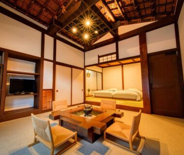 Spacious tatami room with low wooden table, floor chairs, twin beds, shoji screens and exposed wooden ceiling at Shirakabe