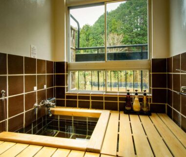 Indoor wooden onsen bath with tiled walls and window view of greenery at Shirakabe, Shizuoka
